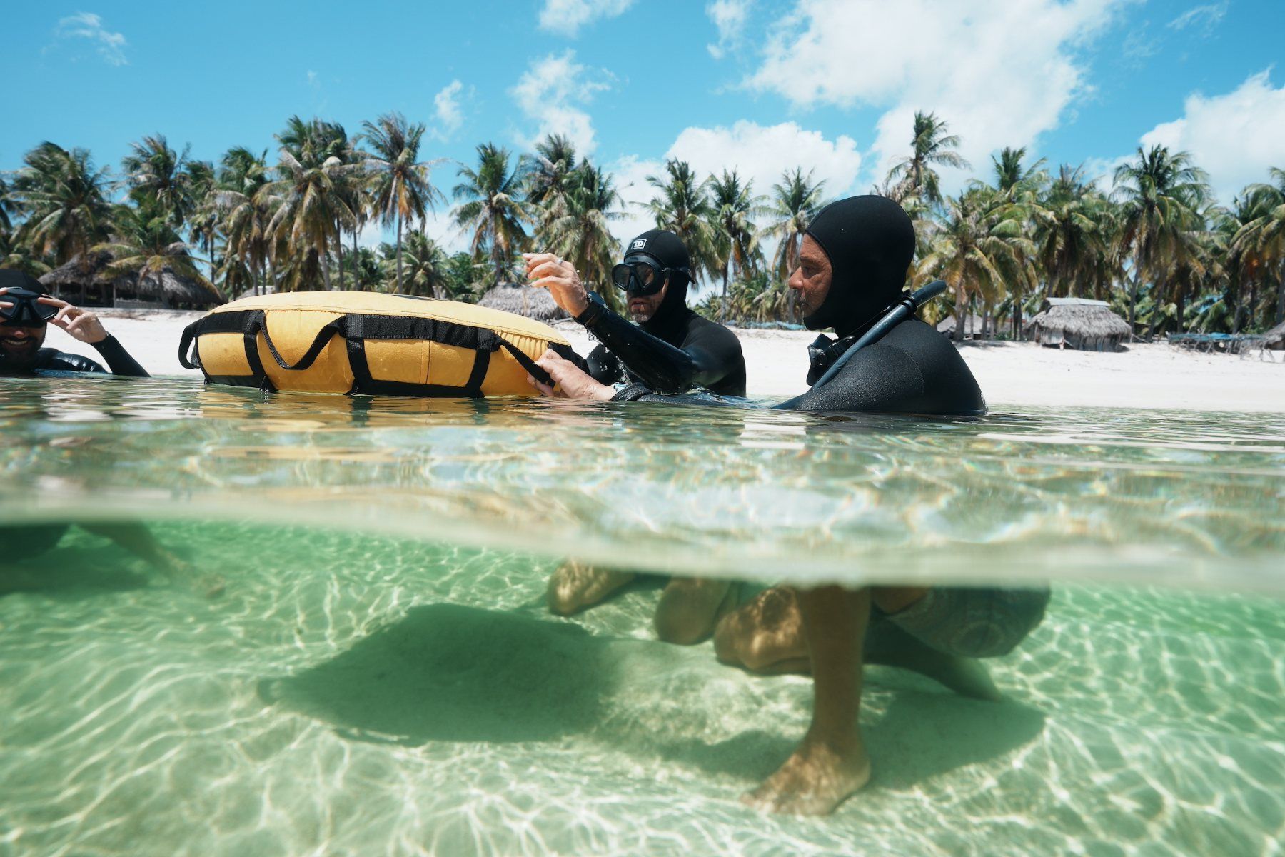 Instructors and a student at the buoy in the shallow lagoon, palms and white sand of Nemberala behind