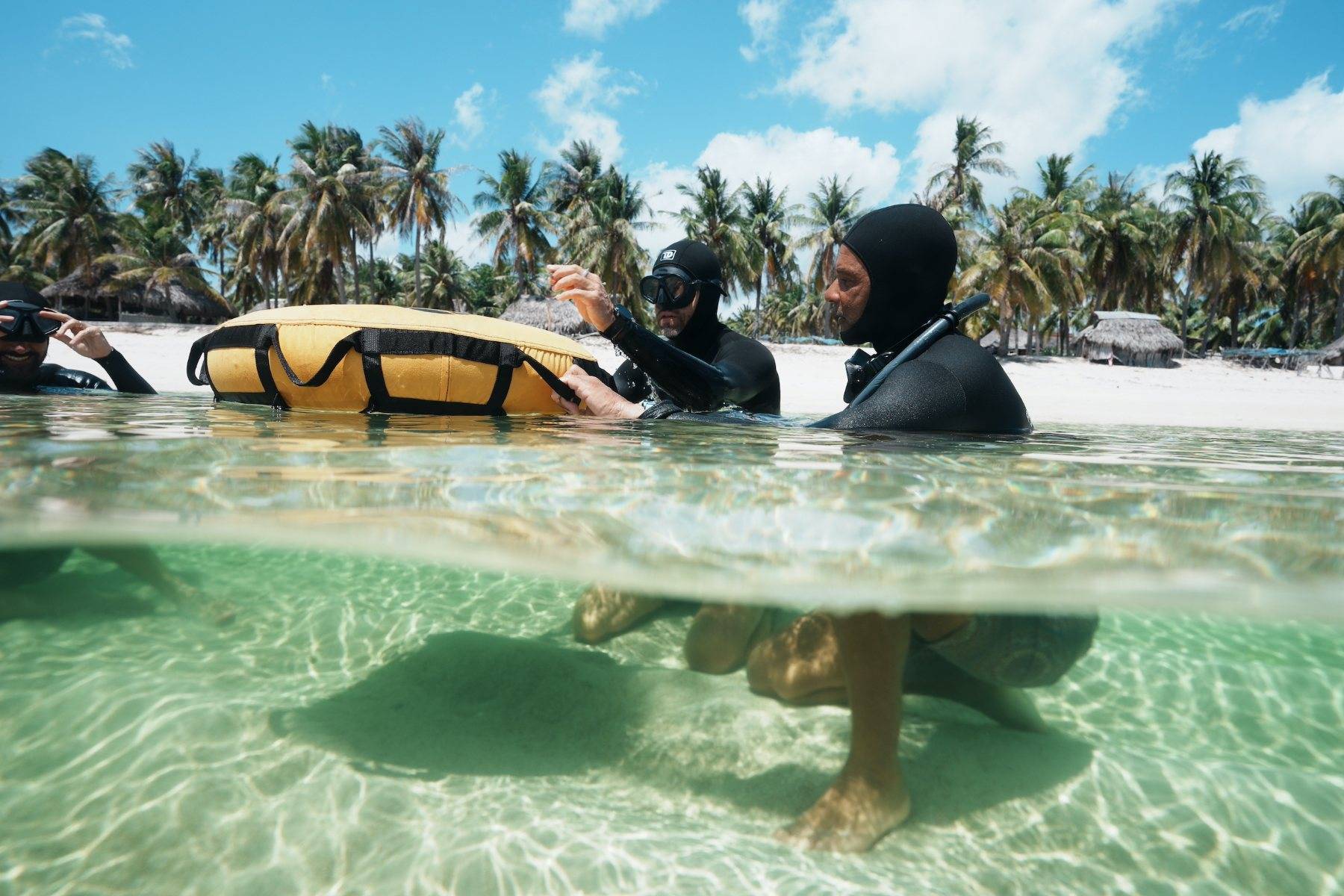 Instructors and a student at the buoy in the shallow lagoon, palms and white sand of Nemberala behind