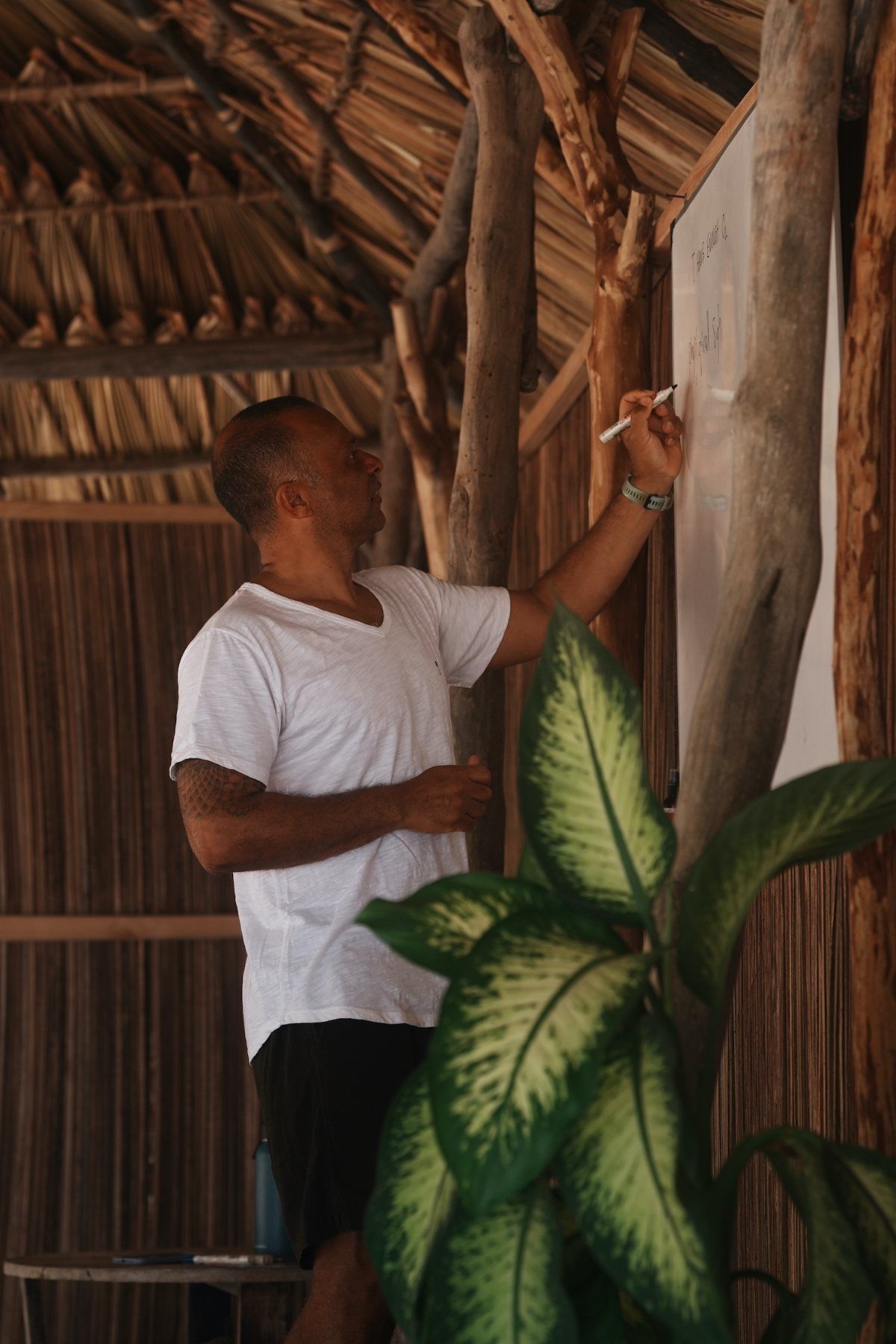 The coach writing session notes on the whiteboard in the palm-thatch shala