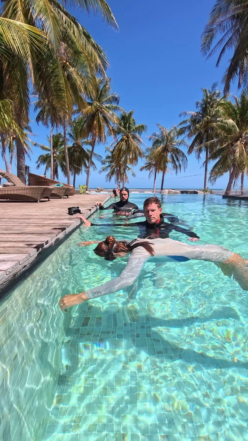 An instructor guiding a student through a relaxed static breath-hold in the palm-fringed pool