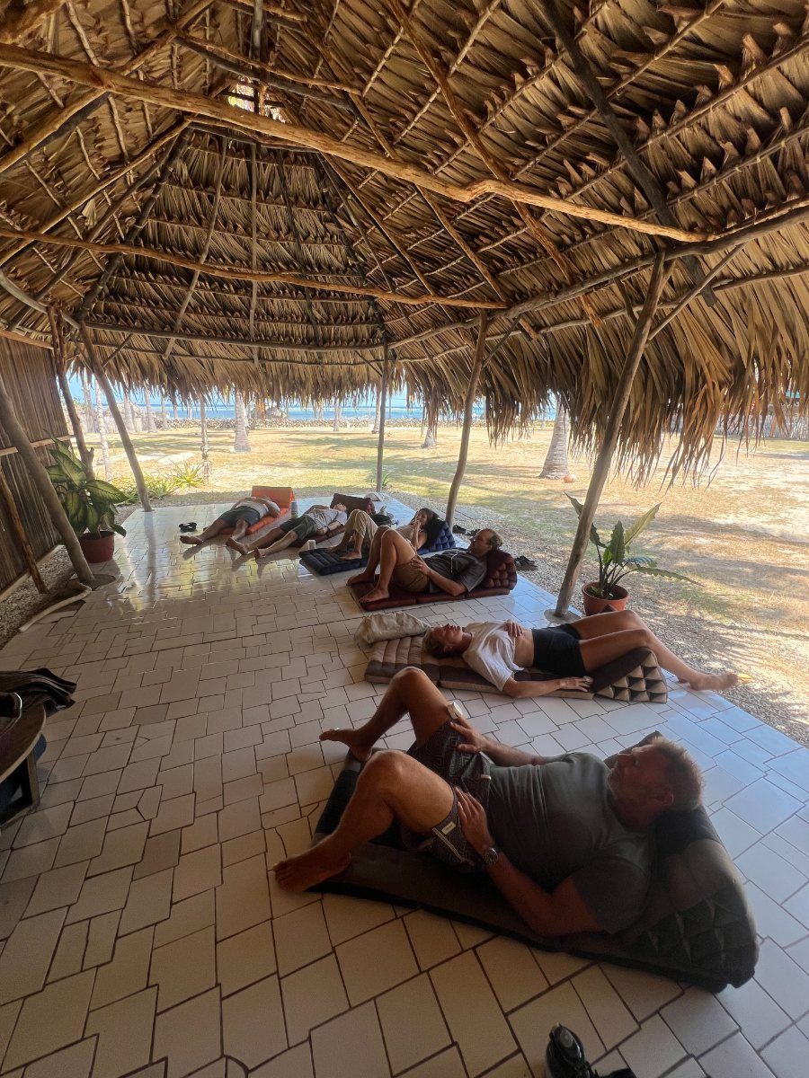 Students resting on cushions in the thatched beachside shala, the lagoon beyond