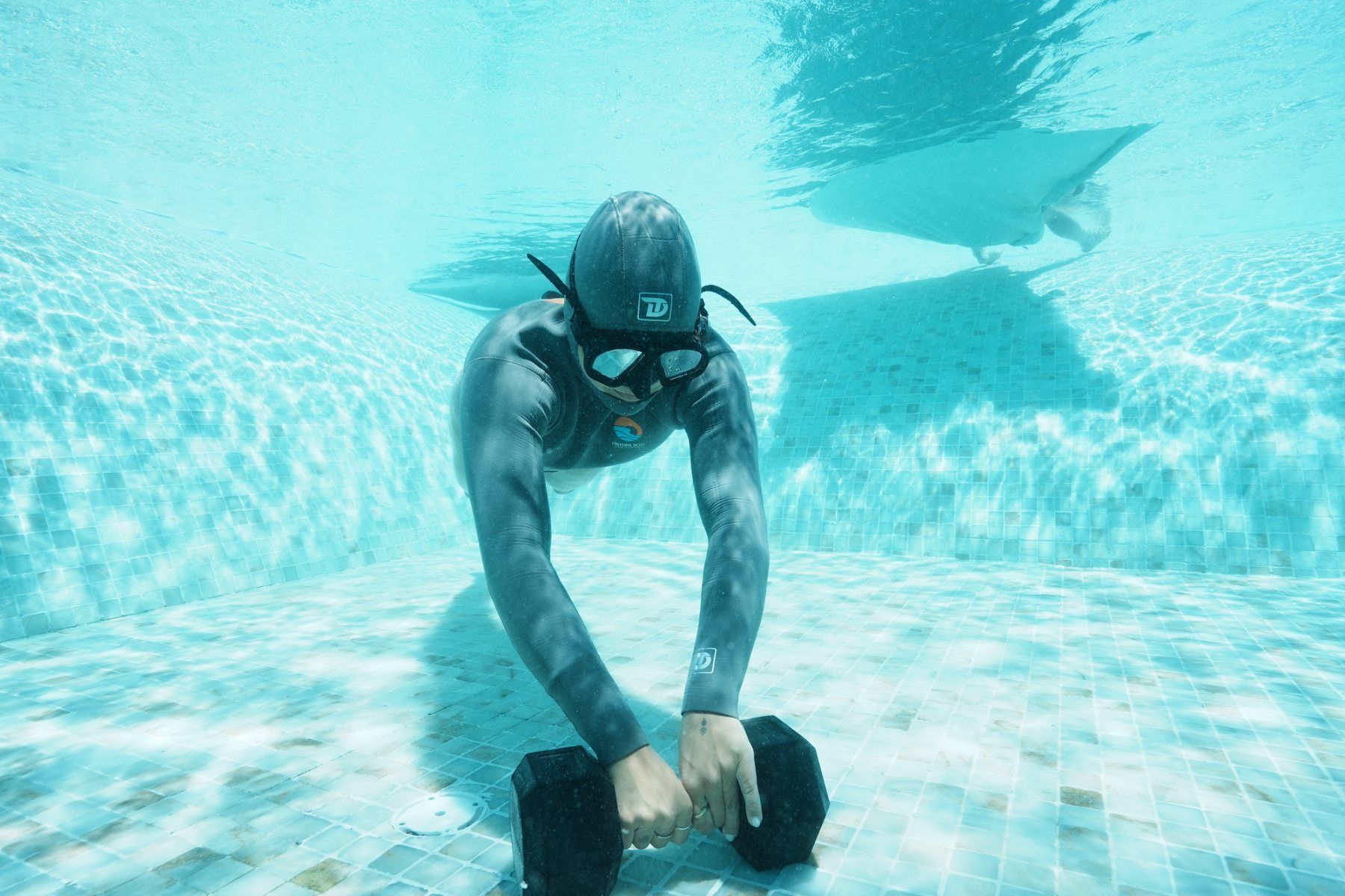 A diver on the pool floor holding a dumbbell during a breath-hold drill