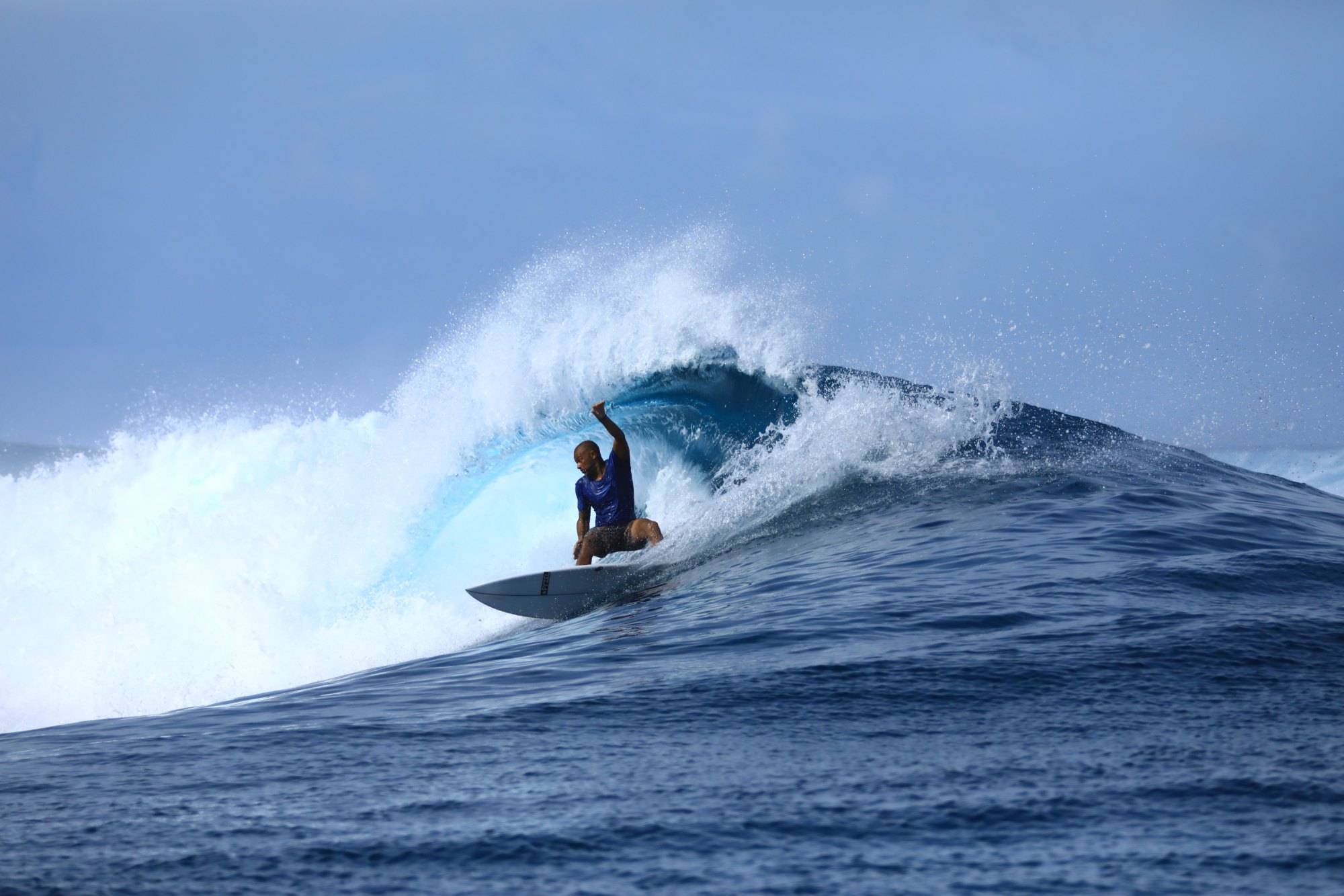 A surfer crouched in the barrel of a heavy blue wave